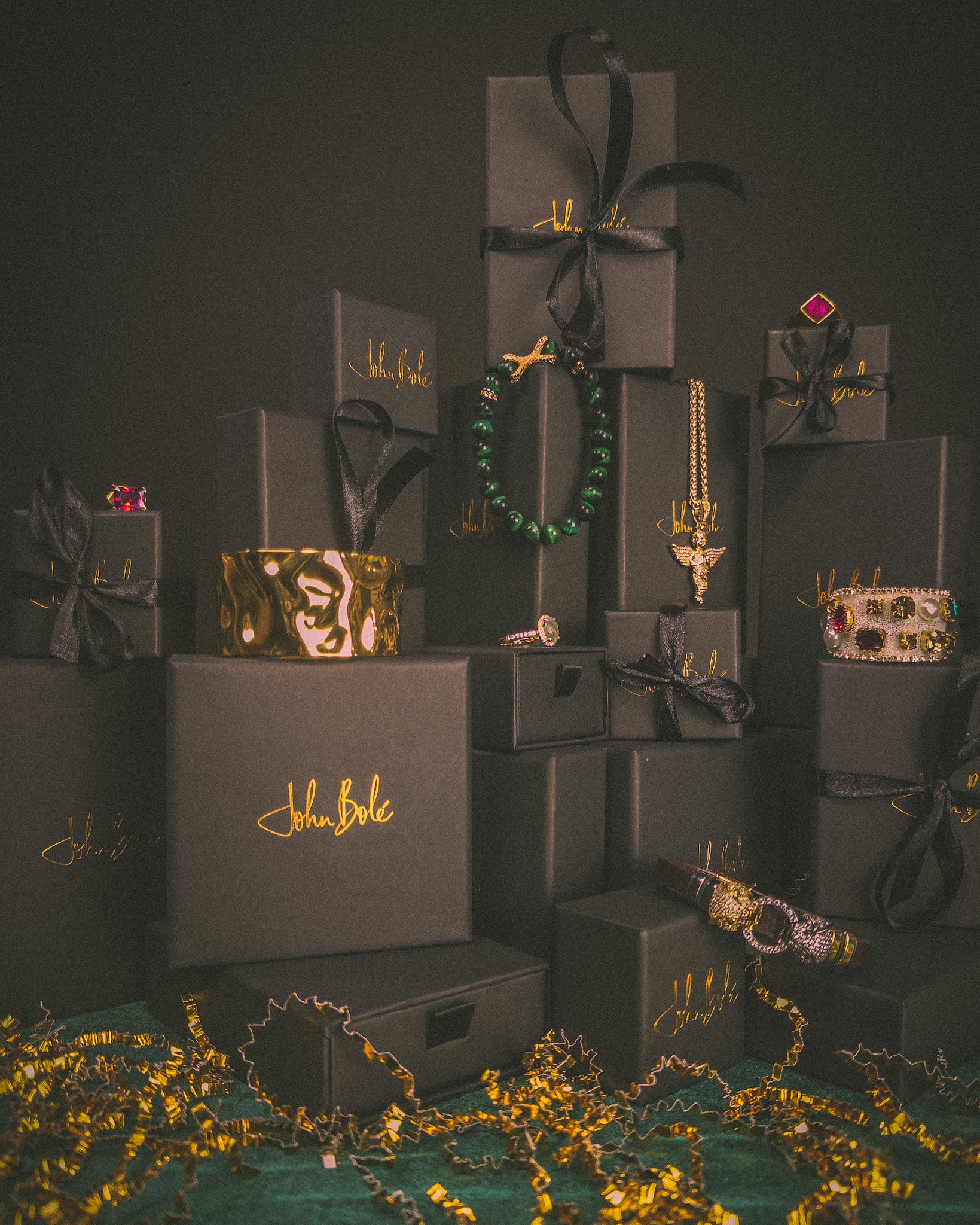 Jewelry displayed on black boxes with 'John Bole' branding against a dark background.

